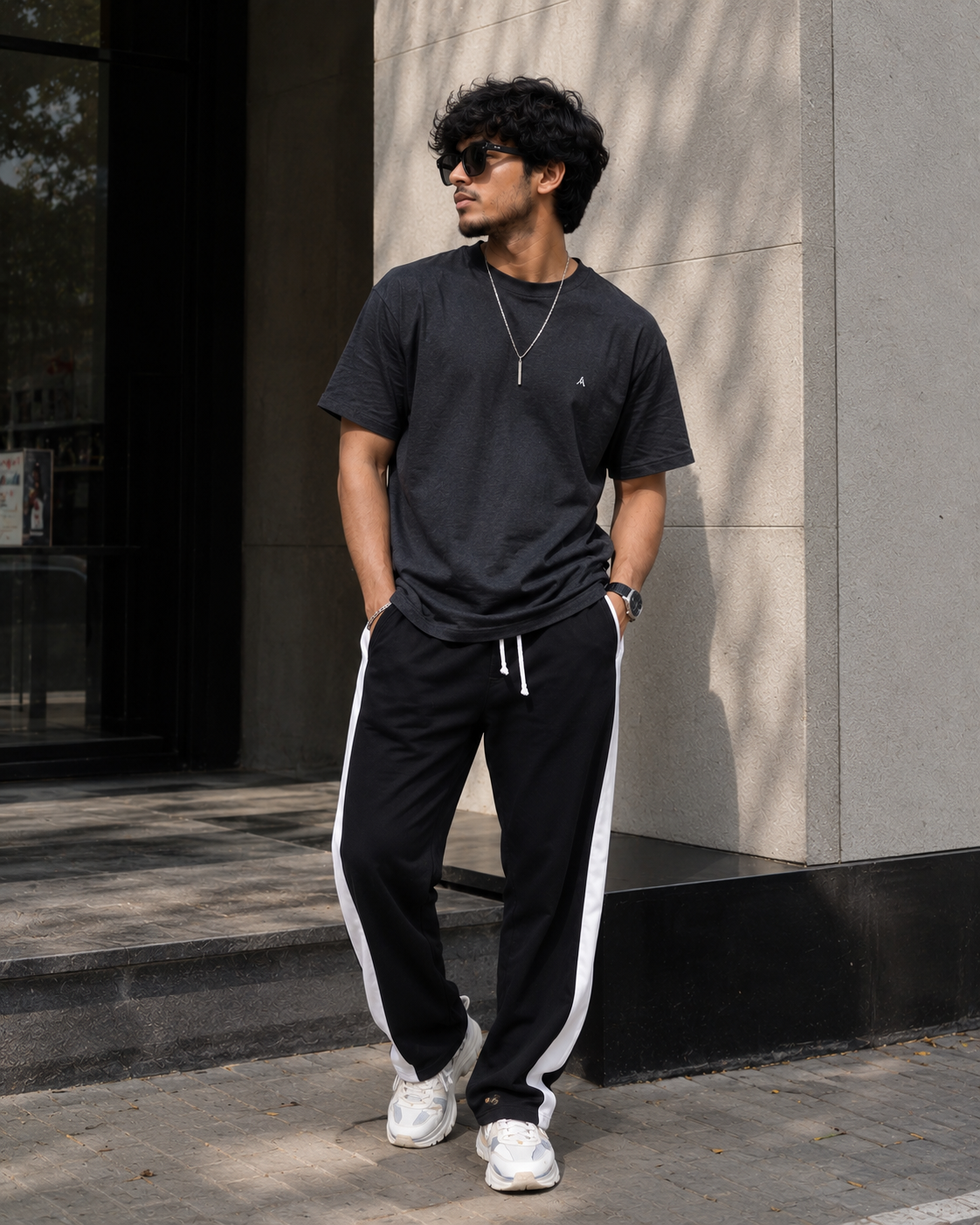 Man wearing a black t-shirt and black pants with white stripes standing against a building.