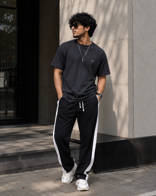 Man wearing a black t-shirt and black pants with white stripes standing against a building.
