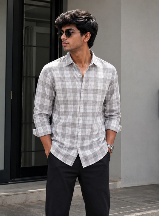 Man wearing a gray checkered shirt and sunglasses standing against a neutral background