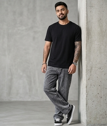 Man wearing a black t-shirt and gray pants leaning against a concrete wall.