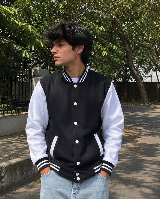Person wearing a black and white varsity jacket outdoors with trees in the background